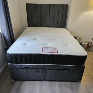 A contemporary beige upholstered Ottoman storage bed with the mattress base lifted by a hydraulic gas-lift mechanism, revealing a large internal storage space.